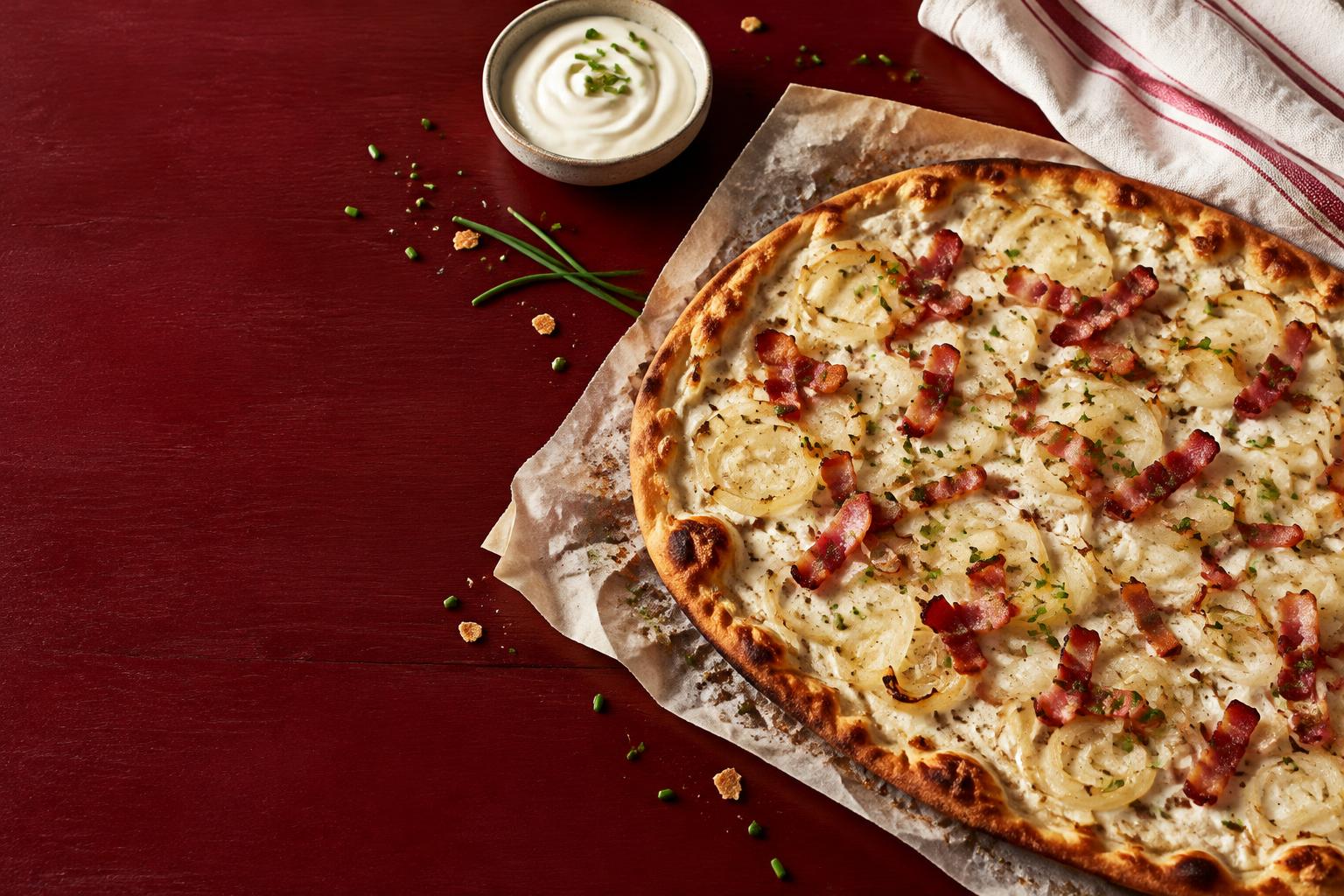 Tarte flambée alsacienne, crème et lardons, sur une table rouge